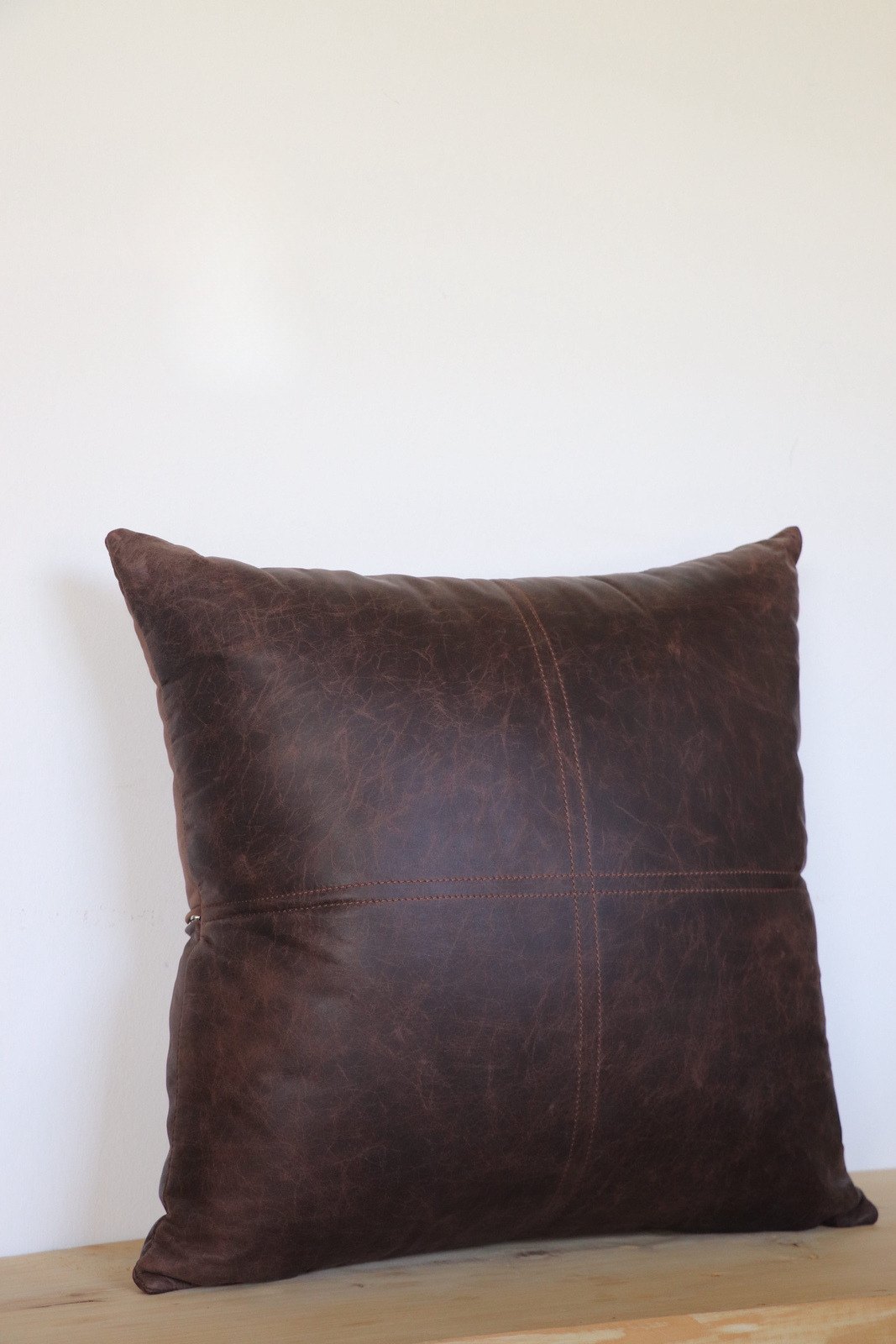 Almohadón de cuero marrón chocolate apoyado sobre una mesa de madera clara